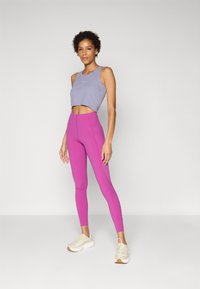 Lila, rövidített tank topp párosítva magasan derékig érő rózsaszín leggingsekkel és bézs sportcipőkkel. A leggingsek sima, elegáns textúrával rendelkeznek.