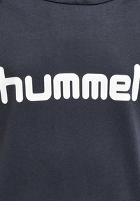Felpa grigia con grande scritta bianca "hummel" sul davanti. Il tessuto ha una finitura liscia ed è dotata di un colletto a girocollo.