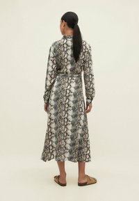 Abito a maniche lunghe, di lunghezza al ginocchio, con un motivo a stampa serpente nero e beige. Il materiale appare liscio; presenta una vita con cintura e colletto da camicia.