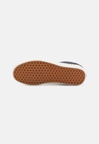 Rubber sole with a honeycomb pattern, featuring a brown color and a white border. Upper made of navy fabric, showing wear around the edges.