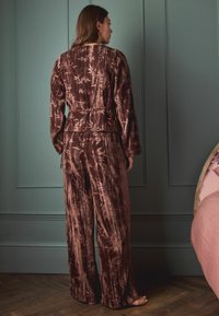 Sammlung aus Samt in Dunkelbraun mit einem strukturierten Bambusdruck. Langärmeliges Oberteil mit Bindeband in der Taille und weit geschnittenen Hosen.