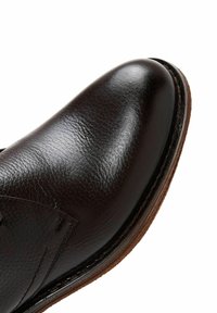 Donkerbruin leren schoen met een glad oppervlak, ronde neus, gedetailleerde stiksels en een tan rubberen zool. Het bovenwerk heeft gestructureerde accenten.
