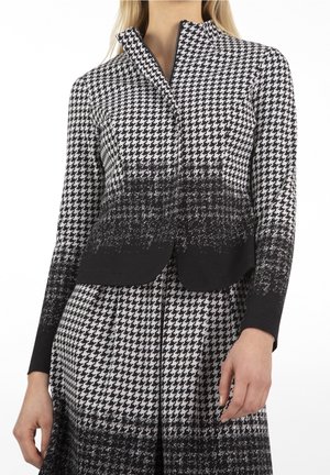 Mujer que lleva una chaqueta y falda con estampado de pata de gallo en blanco y negro con un efecto degradado de negro a blanco.