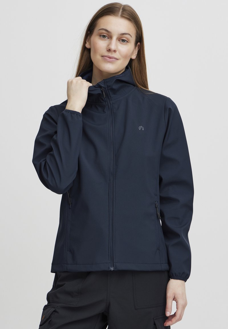 Navy blue softshell jacket with a high collar, zippered front, and side pockets. Features elastic cuffs and a minimalist logo on the chest.