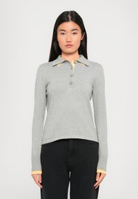 Polo à manches longues gris avec un accent jaune sur le col, dotée d'un boutonnage et de poignets côtelés. Tissu doux, coupe décontractée.