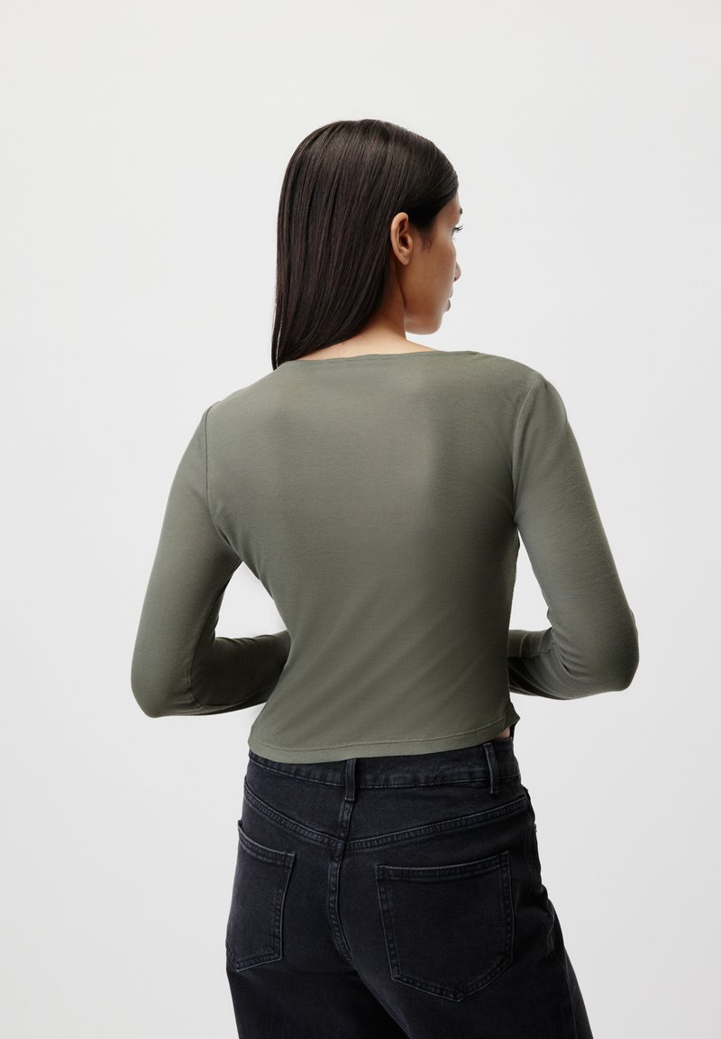 Maglia a maniche lunghe di colore verde oliva, realizzata in tessuto morbido, con scollo rotondo e design cropped, abbinata a jeans neri a vita alta.