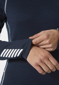 Granatowa koszulka z długim rękawem, wykonana z miękkiej, teksturowanej tkaniny. Posiada białe akcenty w szwie oraz paski na mankietach.