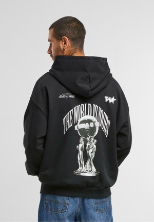 Zwarte hoodie met een grafisch ontwerp op de achterkant met de tekst "DE WERELD IS VAN JOU," vergezeld van geïllustreerde figuren en een wereldbolontwerp.