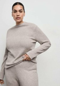 Beige, lange mouw pullover gemaakt van zachte stof, met een hoge hals en een comfortabele pasvorm, gecombineerd met bijpassende broek. Eenvoudig ontwerp, zonder patronen.