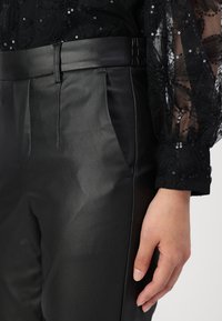 Pantalones de imitaci�ón cuero negros con una textura suave, que presentan un ajuste a medida, bolsillos laterales y un acento brillante en la cintura.
