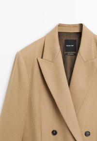 Kamelbrauner, doppelt geknöpfter Wollblazer mit Reverskragen, schwarzen Knöpfen und glatter Textur. Label "Massimo Dutti."