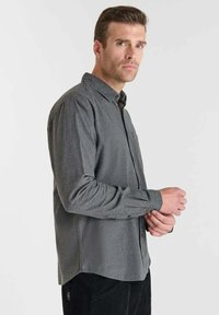 Camisa gris de manga larga con cuello abotonado, hecha de una tela suave, con dobladillo recto y corte relajado. Sin patrones ni acentos visibles.