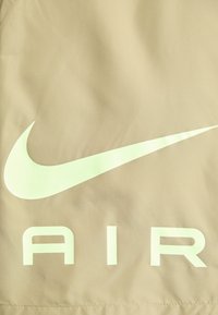 Beige jas met een zachte textuur, voorzien van een groot lichtgroen Nike swoosh-logo en het woord "AIR" in vette, ook lichtgroene letters.