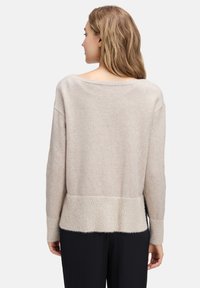 Jasno beżowy sweter o luźnym kroju, z szerokim dekoltem i ściągaczem na dolnym brzegu. Materiał wydaje się być miękki i teksturowany.