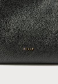 Melnas teksturētas ādas maks ar zelta "FURLA" logotipu. Materiāls ir graudains ar redzamu tekstūru un mīkstu apdari.