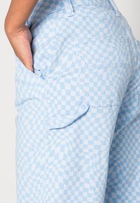 As calças xadrez azul claro apresentam uma superfície texturizada, bolsos laterais e detalhes de costura visíveis ao longo dos bolsos e da cintura.