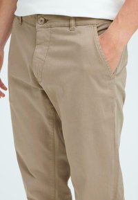 Beige cotton chinos with a slim fit, featuring side pockets, a zip fly, and a single-button closure, smooth texture and minimal stitching detail.