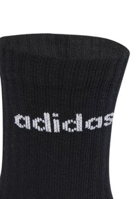 Calcetín negro de punto con textura acanalada, que presenta el texto en blanco "adidas" a lo largo del lado. Longitud estándar de caña.