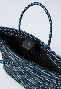 Modrá, černá a béžová tkaná kabelka s kulatými rukojetmi a černým vnitřkem, který obsahuje magnetické zapínání a vnitřní kapsu.