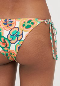 Többszínű virágmintás bikini alsó. Rugalmas anyagból készült, oldalt megkötős részletekkel és alacsonyabb derékvonallal. Sima textúra.