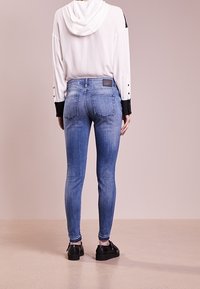 Vaqueros skinny azules con una textura desgastada, combinados con una sudadera blanca que presenta detalles en negro. Los vaqueros tienen un bolsillo trasero y una etiqueta.