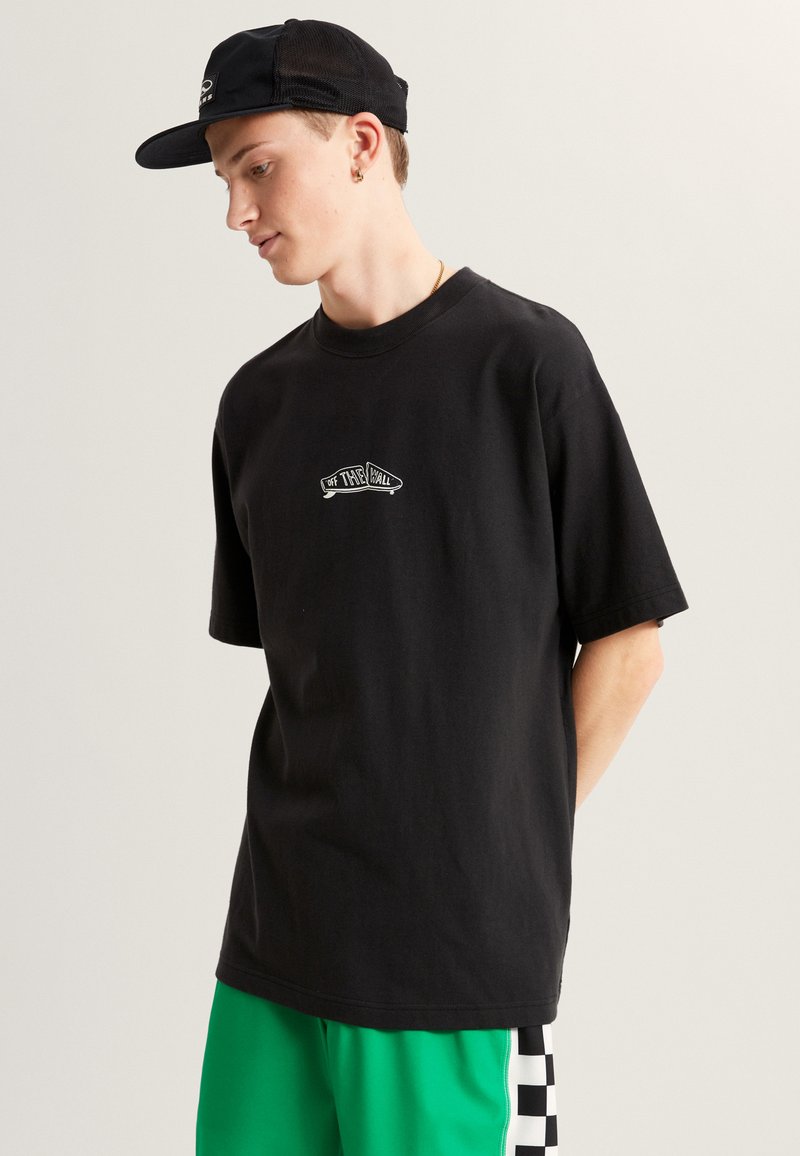 Zwarte katoenen t-shirt met korte mouwen, voorzien van een witte "Off the Wall" logo in een curve ontwerp op de voorkant, gecombineerd met contrasterende groene shorts.