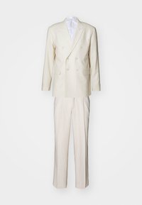 Chaqueta de traje de doble botonadura en color crema con solapas, acompañada de pantalones rectos a juego. Textura suave, corte a medida.