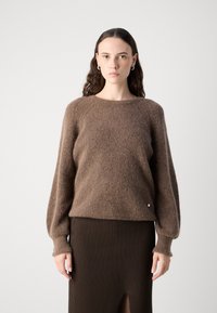 Pulover tricotat, de culoare maro, cu textură ribată, guler rotund și mâneci ușor bufante. Prezintă un detaliu mic de accent auriu.
