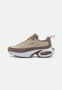 Chaussure de sport beige et marron avec une tige en mesh lisse, une semelle intermédiaire blanche épaisse, une unité d'air visible et un design à bout arrondi.