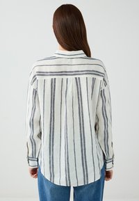 Hemd mit Knopfleiste aus leichtem, gestreiftem Stoff. Cremefarbener Hintergrund mit marineblauen vertikalen Streifen. Lässige Passform mit abgerundetem Saum und Kragen.