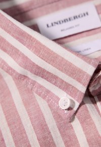Camicia a righe in lino rosa chiaro e bianco sporco, con colletto a punta e un bottone bianco. La texture è leggermente ruvida.