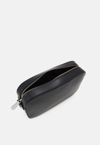 Pochette in pelle nera con forma rettangolare arrotondata, caratterizzata da una zip dorata e una superficie texturizzata. L'interno non foderato è visibile.