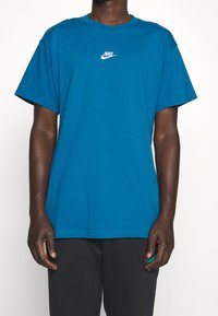 Tyrkysové bavlněné tričko s kulatým výstřihem a krátkými rukávy, s malým bílým logem Nike na hrudi. Texturovaná tkanina.