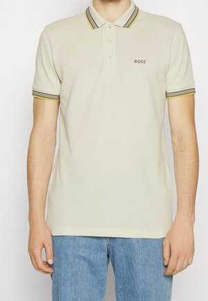 Polo-Shirt aus leichtem beigen Baumwollmaterial mit einer Drei-Knopf-Leiste. Schwarze und gelbe gestreifte Rippkragen- und Ärmelakzente. Dezentes gesticktes "BOSS"-Logo.