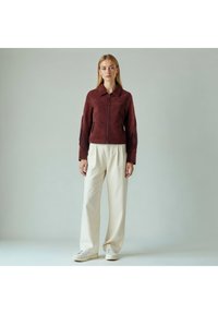 Bordeaux ruskindsjakke med frynser på ærmerne, lynlås og spids krave; kombineret med lyse cremefarvede bukser og hvide sneakers.