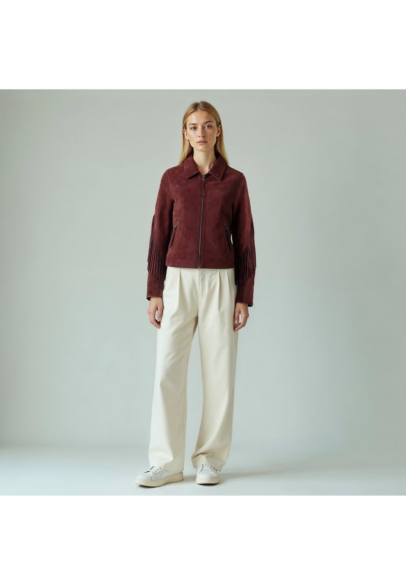 Bordeaux ruskindsjakke med frynser på ærmerne, lynlås og spids krave; kombineret med lyse cremefarvede bukser og hvide sneakers.