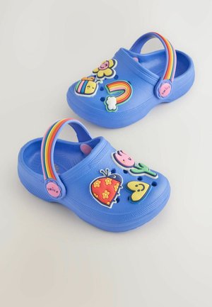 Zoccoli di plastica blu con colorati charm decorativi in 3D: fiori, una coccinella, un arcobaleno e faccine sorridenti; cinturino arcobaleno regolabile.