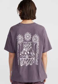 Paarse katoenen t-shirt met een witte grafische print op de achterkant, inclusief zonnen, bergen en tekst die leest "FROZEN WAVE CULT."