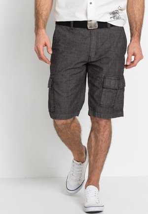 Shorts cargo gris charbon avec plusieurs poches, une coupe droite et des ourlets, associés à des baskets blanches et une chemise à boutons.