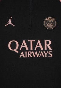 Fekete sportfelső negyedcipzárral, rózsaszín hímzéssel a Jumpman logóval, valamint a "QATAR AIRWAYS" felirattal és egy kerek PSG logóval.