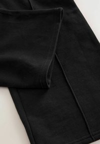 Tissu noir plié avec des lignes de couture visibles, présentant une texture douce et une couture propre sur une surface claire.