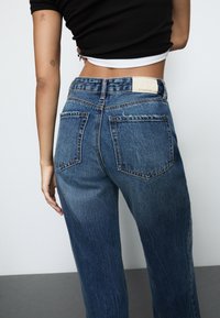 Modre visokotrzne kavbojke z ravnim nogama, z zbledele pranje, petimi žepi in označeno etiketo na hrbtnem pasu.