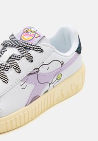 Weißer Sneaker mit strukturiertem Plattformsohle, schwarz-weißen Schnürsenkeln und einem Snoopy-Design an der Seite, ergänzt durch lila Akzente und ein buntes Etikett.