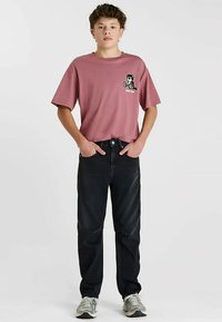 Roze katoenen T-shirt met korte mouwen en een zwart berenafbeelding op de linkerborst, gecombineerd met donkere spijkerbroek en grijze sneakers.