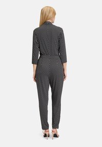 Svart jumpsuit med ett geometriskt vitt mönster, som har krage, trekvartslånga ärmar, en åtsittande midja och smalnade ben.