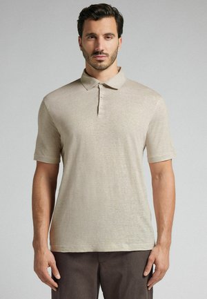 Beige polo shirt med en blød tekstur, kortærmer og en tre-knaplukning. Båret af en mandlig model på en neutral baggrund.