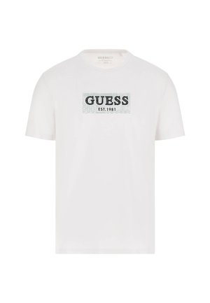 White cotton t-shirt featuring a rectangular black "GUESS" logo with "EST. 1981" underneath, set against a textured light blue background.