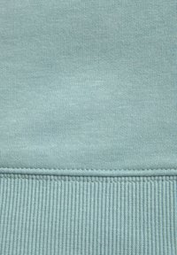 Himmelblaues Fabrik mit einer weichen Textur; verfügt über einen gerippten Saum und eine Naht am unteren Rand, die einen nahtlosen Übergang zwischen den Texturen schafft.