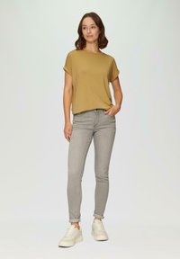 Jasno musztardowa koszulka z krótkim rękawem z podwiniętymi mankietami, zestawiona z szarymi skinny jeansami i białymi sneakersami. Prosty i schludny design.