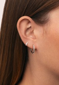 Pendientes de aro de plata mostrados en una oreja, uno con un acabado suave y el otro adornado con pequeñas gemas claras.